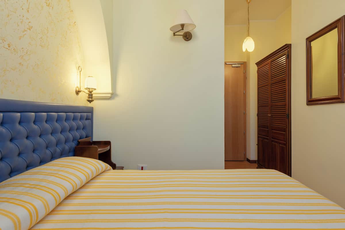 Habitación de hotel con cabecera acolchada, colcha a rayas, lámpara de pared y armario de madera.