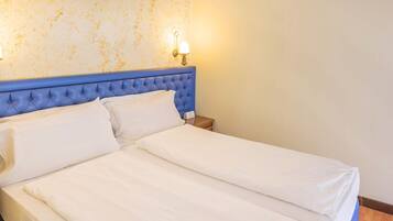 Una cama con cabecera azul, ropa de cama blanca y una pared con textura decorativa.
