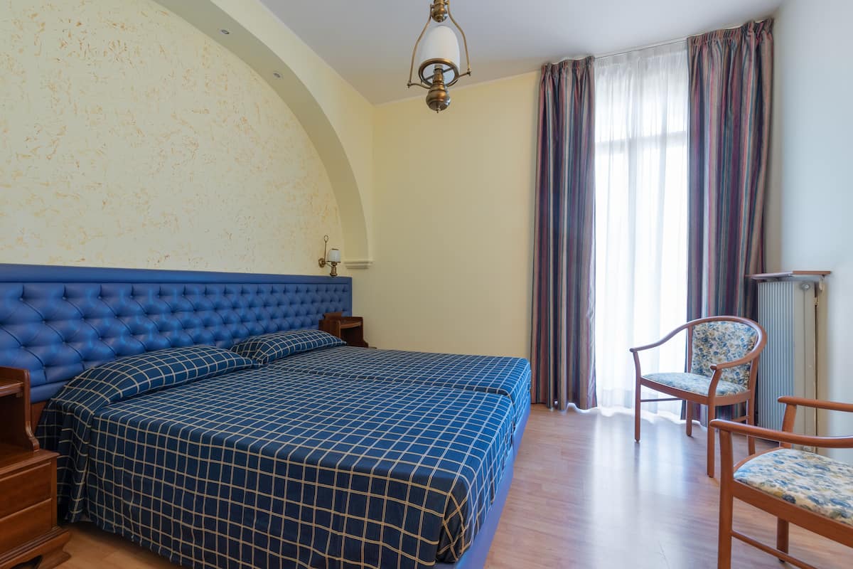 Un dormitorio con una cama grande, una mesita de noche de madera, una silla y una ventana con cortinas.