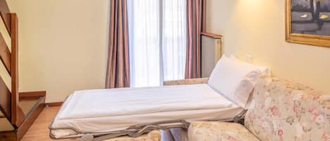 A hotel room with a bed, a sofa, a window with curtains, and a painting on the wall.