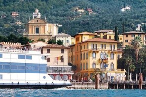A waterfront building with a large white boat docked in front. - Hotel Malcesine (Malcesine)