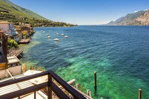 A coastal view with clear blue water, boats, and a building with a balcony overlooking the sea. - Hotel Malcesine (Malcesine)