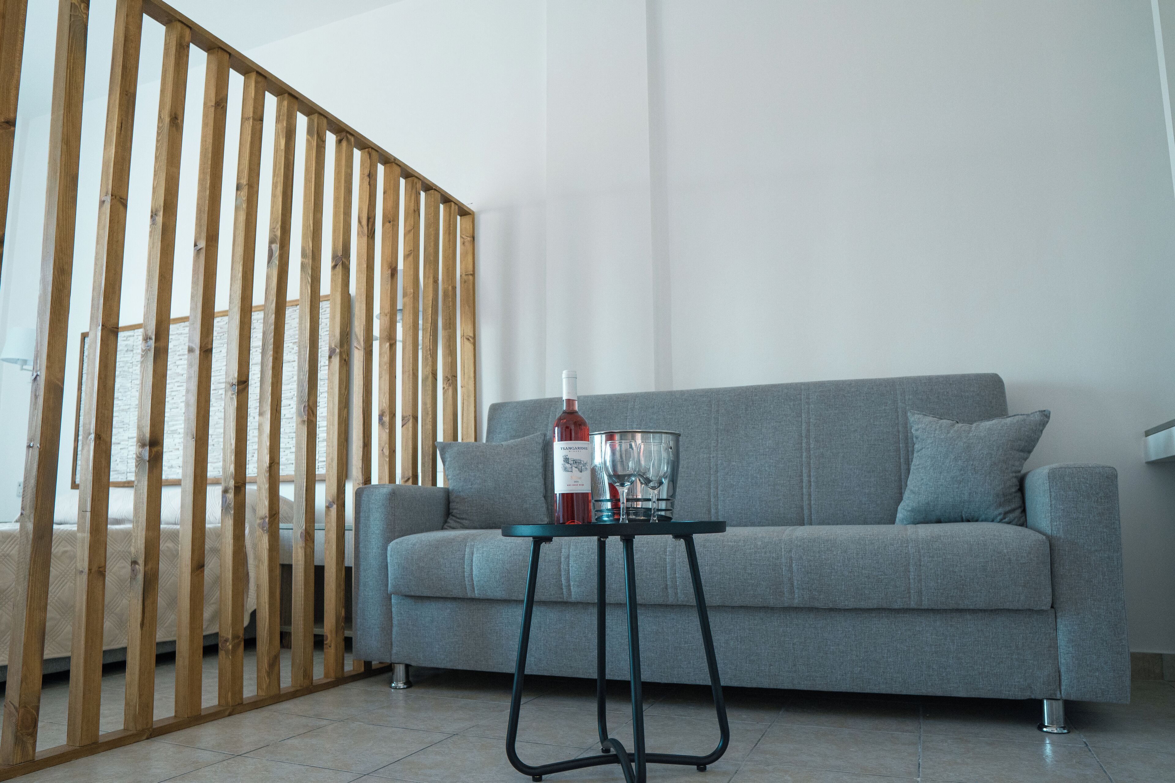 Una sala de estar moderna con un sofá gris, un separador de madera y una mesita con una botella y vasos.
