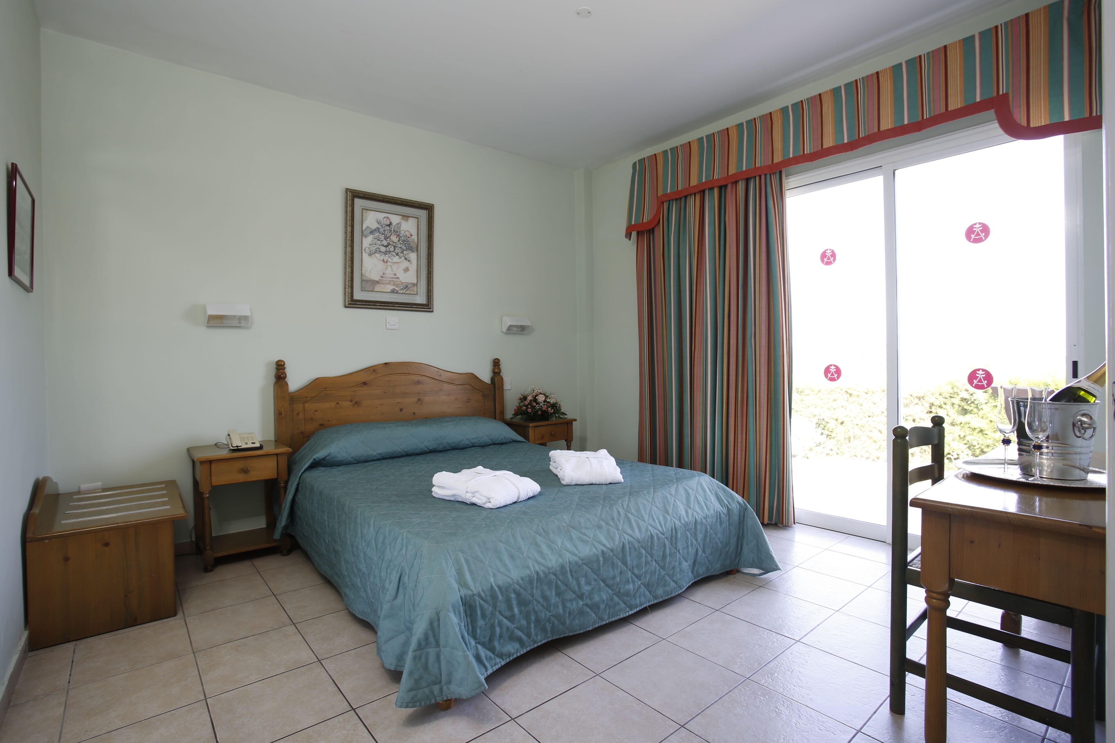 Un dormitorio con cama, mesita de noche, silla y ventana con cortinas.