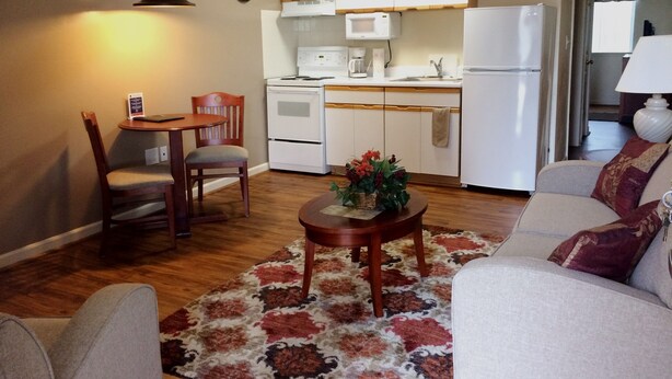 A living room with a sofa, a coffee table with a plant, a dining area with a table and chairs, and a kitchen with white cabinets and appliances.