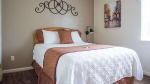 A neatly made bed with a patterned bedspread, a wall-mounted decorative piece, and a painting on the wall.