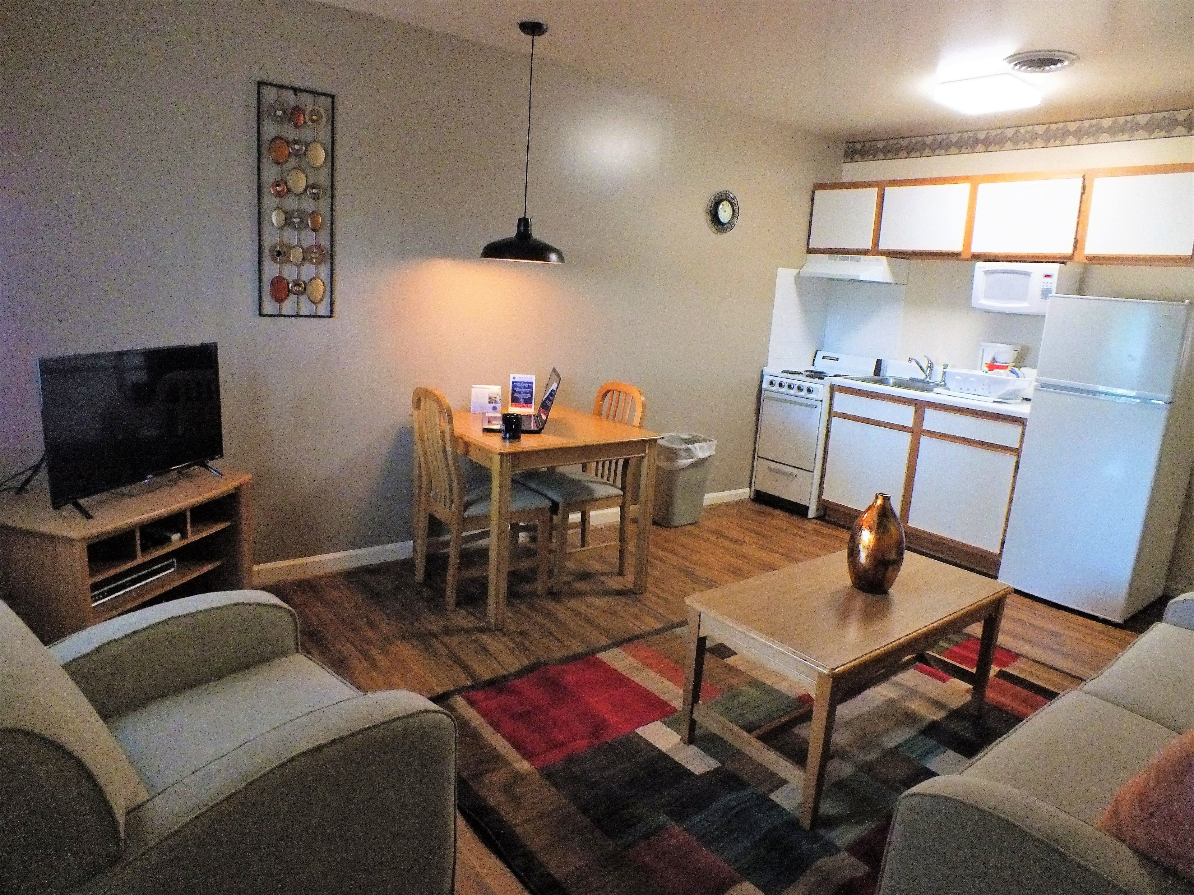 A compact living space with a TV, dining table, chairs, a sofa, a coffee table, a kitchen with a stove, microwave, and refrigerator.
