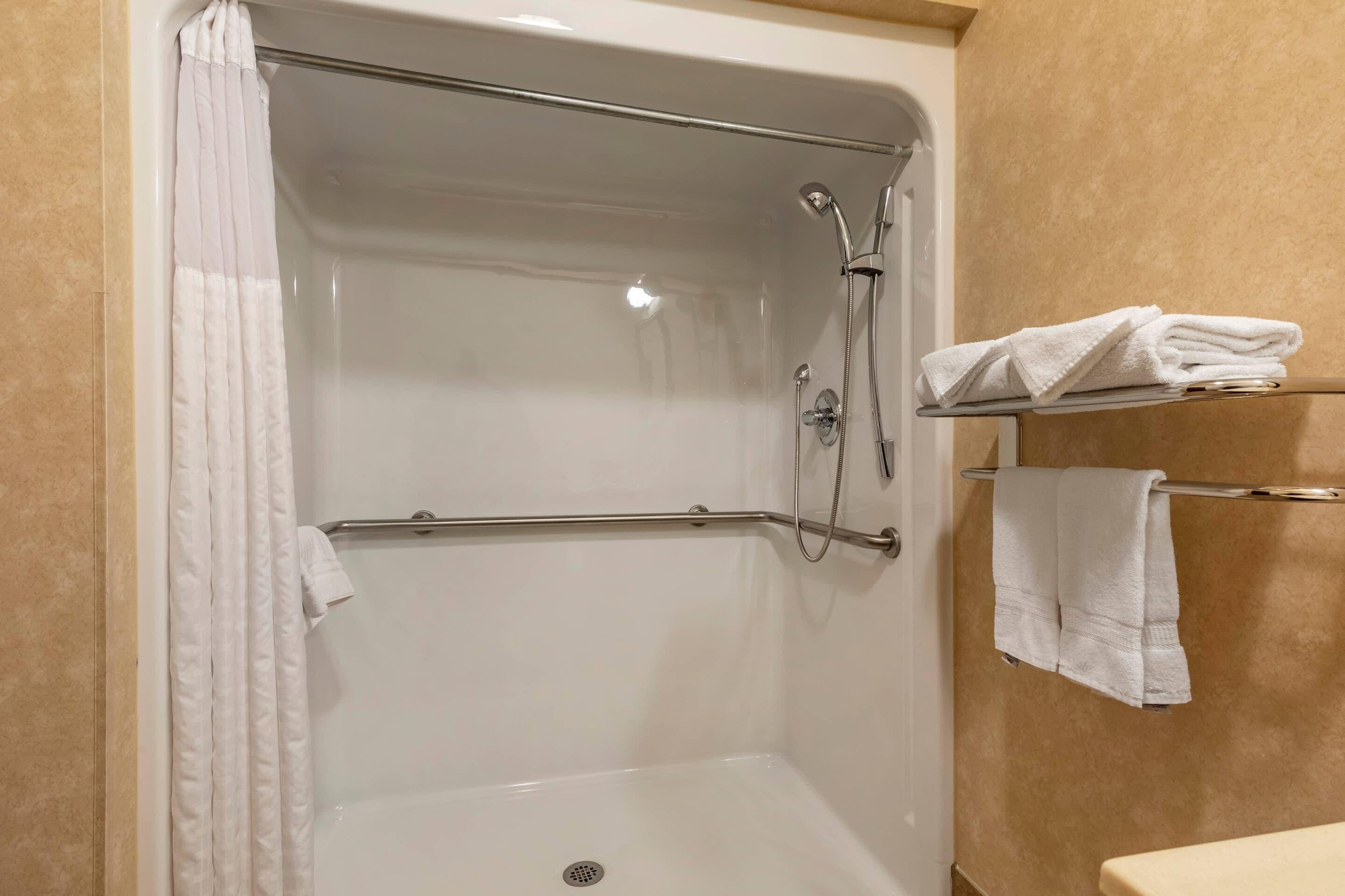 A shower area with a glass door, a handrail, and a towel rack with folded towels.