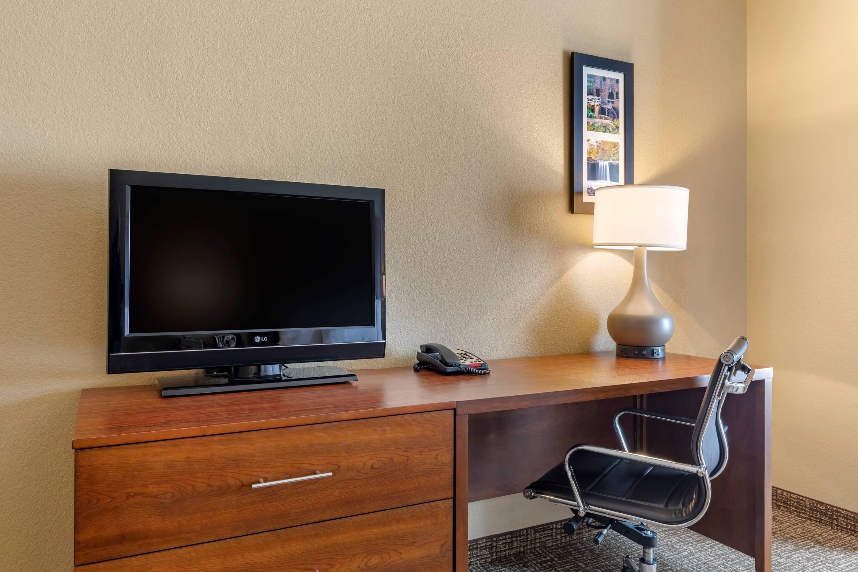 A hotel room with a wooden desk, a television, a lamp, a chair, and a phone.