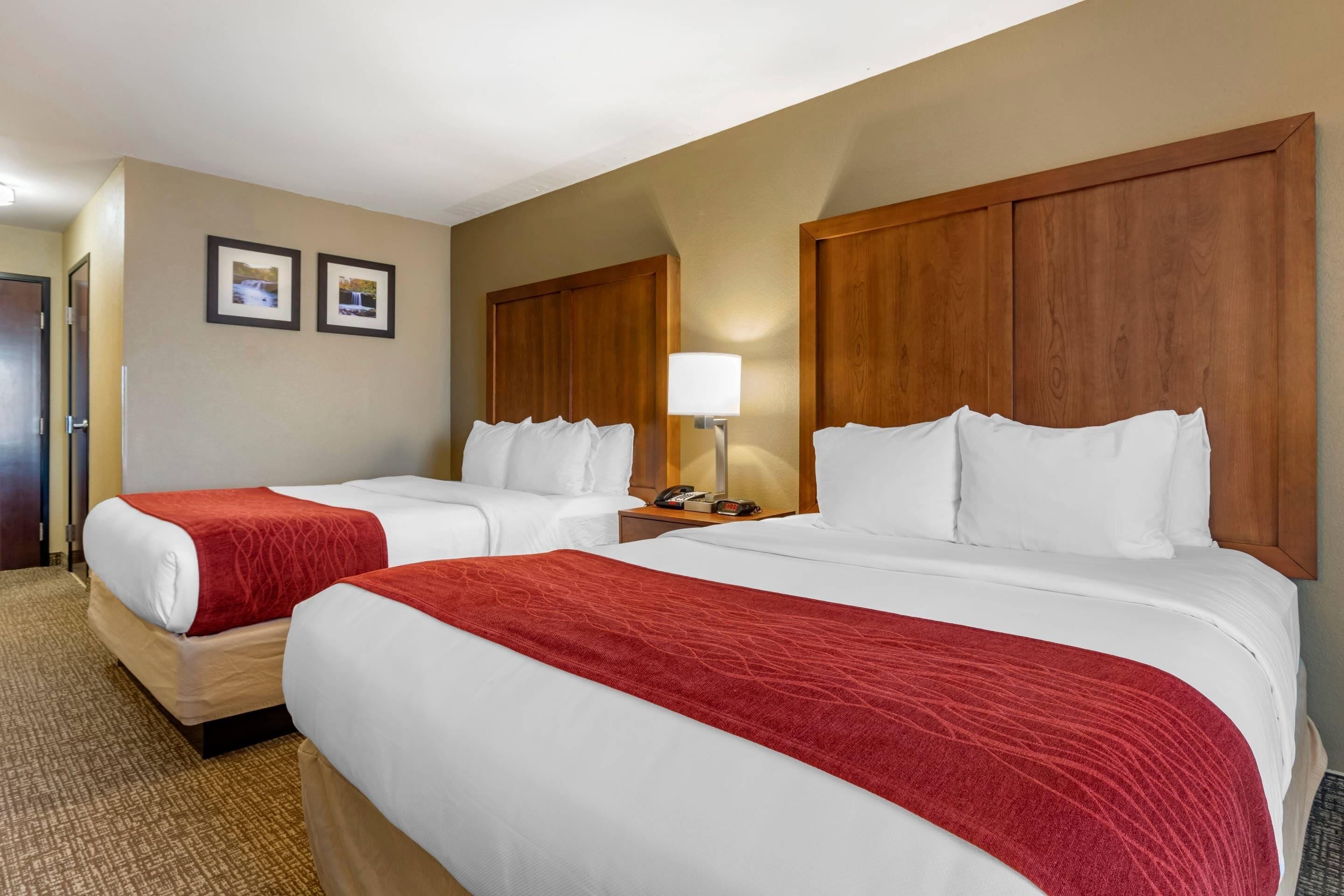 A hotel room with two beds, a nightstand with a lamp, and two framed pictures on the wall.