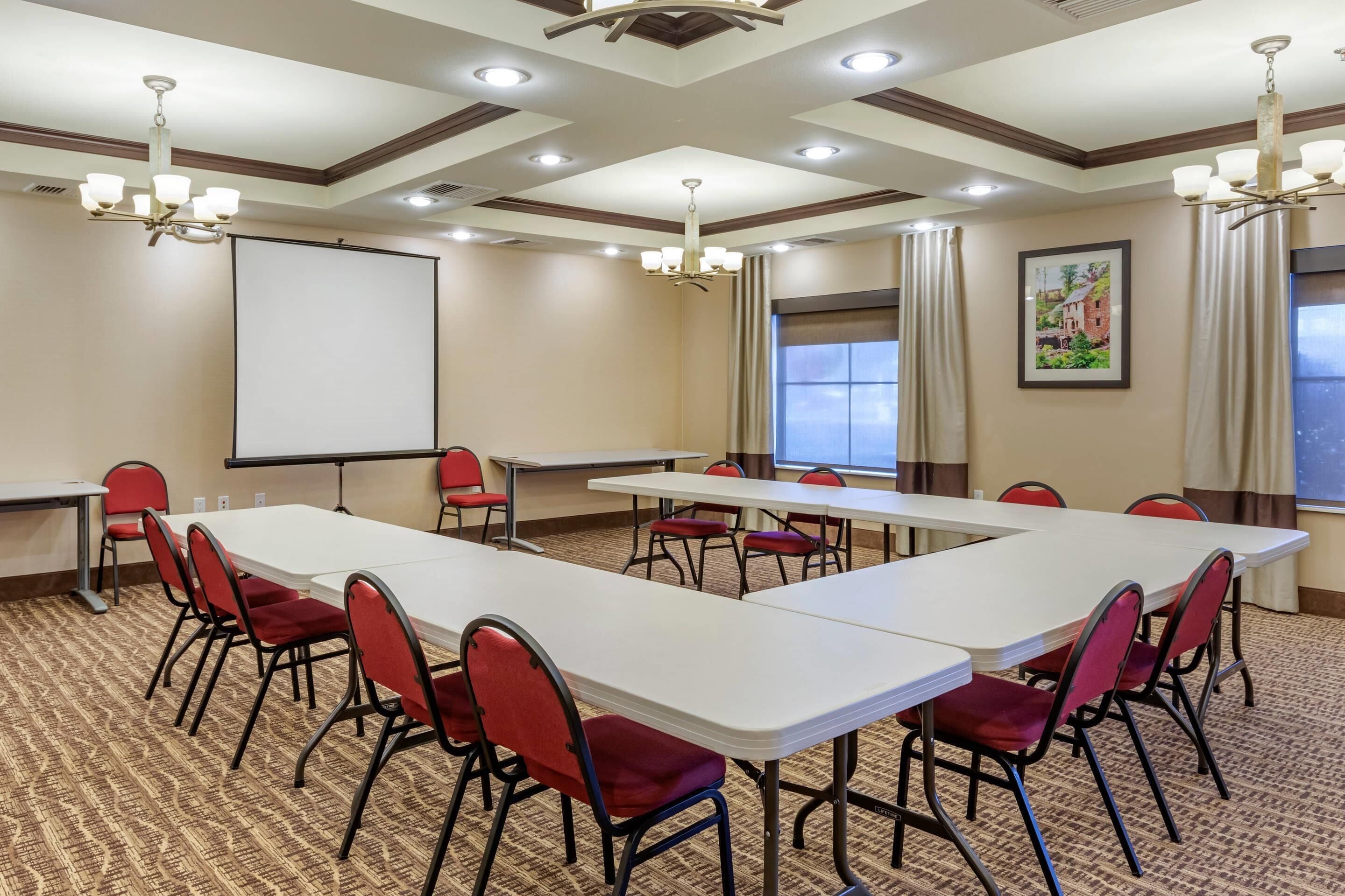 A conference room with a large table, red chairs, a projector screen, and a large window.