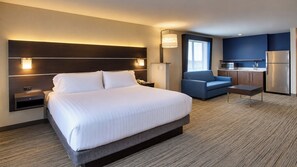 Una habitación de hotel con una cama grande, un escritorio, una silla, una kitchenette y una ventana.
