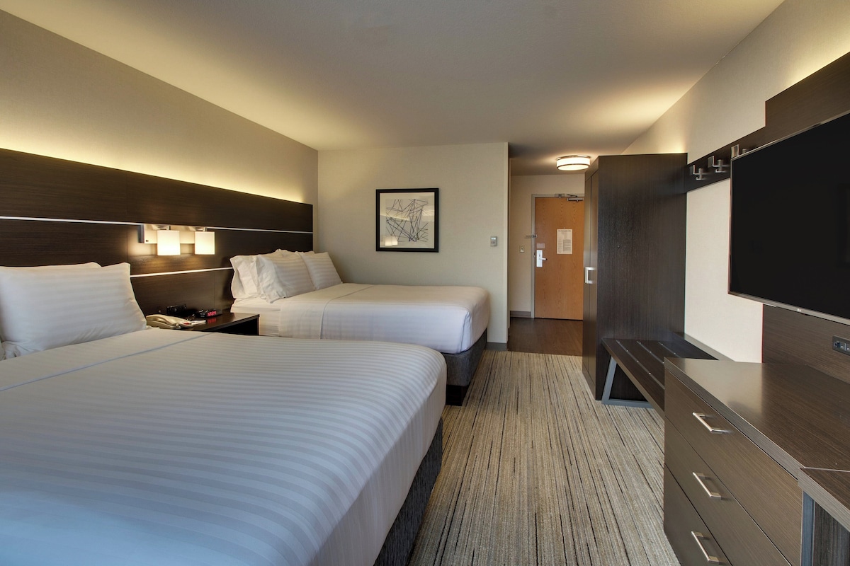 Habitación de hotel con dos camas, un televisor de pantalla plana, una lámpara de pared y una puerta que da a otra habitación.