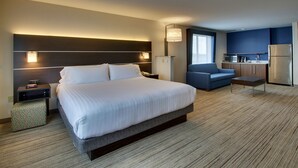 Une chambre d’hôtel avec un grand lit, un bureau, une chaise, une kitchenette et une fenêtre.