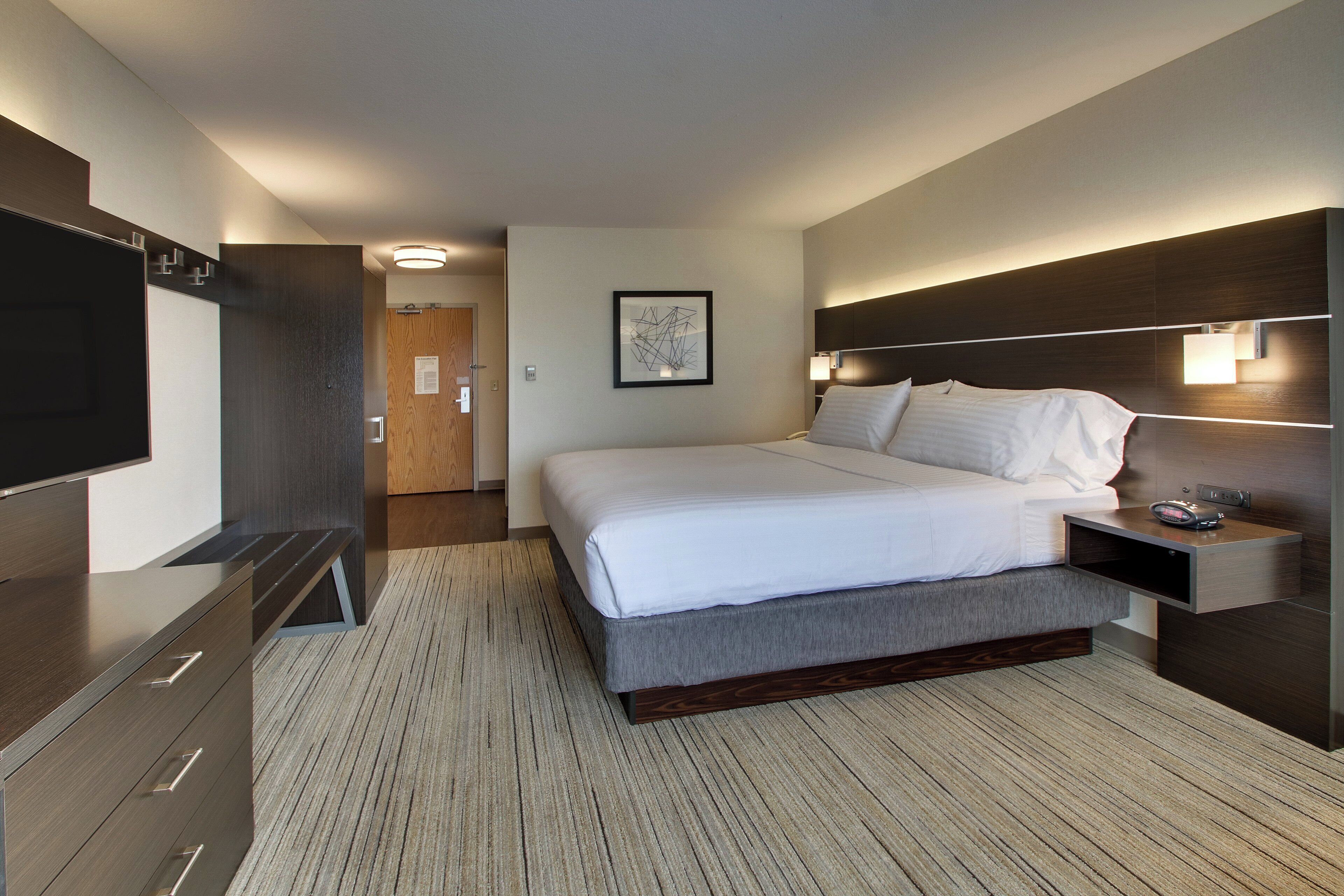 Une chambre d’hôtel moderne avec un grand lit, des tables de chevet, un téléviseur à écran plat et une porte en bois.