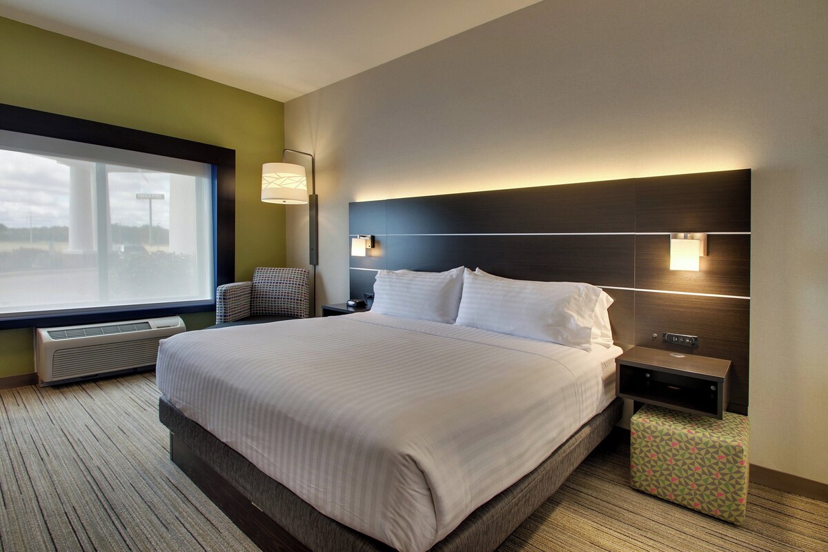 Une chambre d’hôtel avec un grand lit, une table de chevet, une lampe et une vue sur l’extérieur.