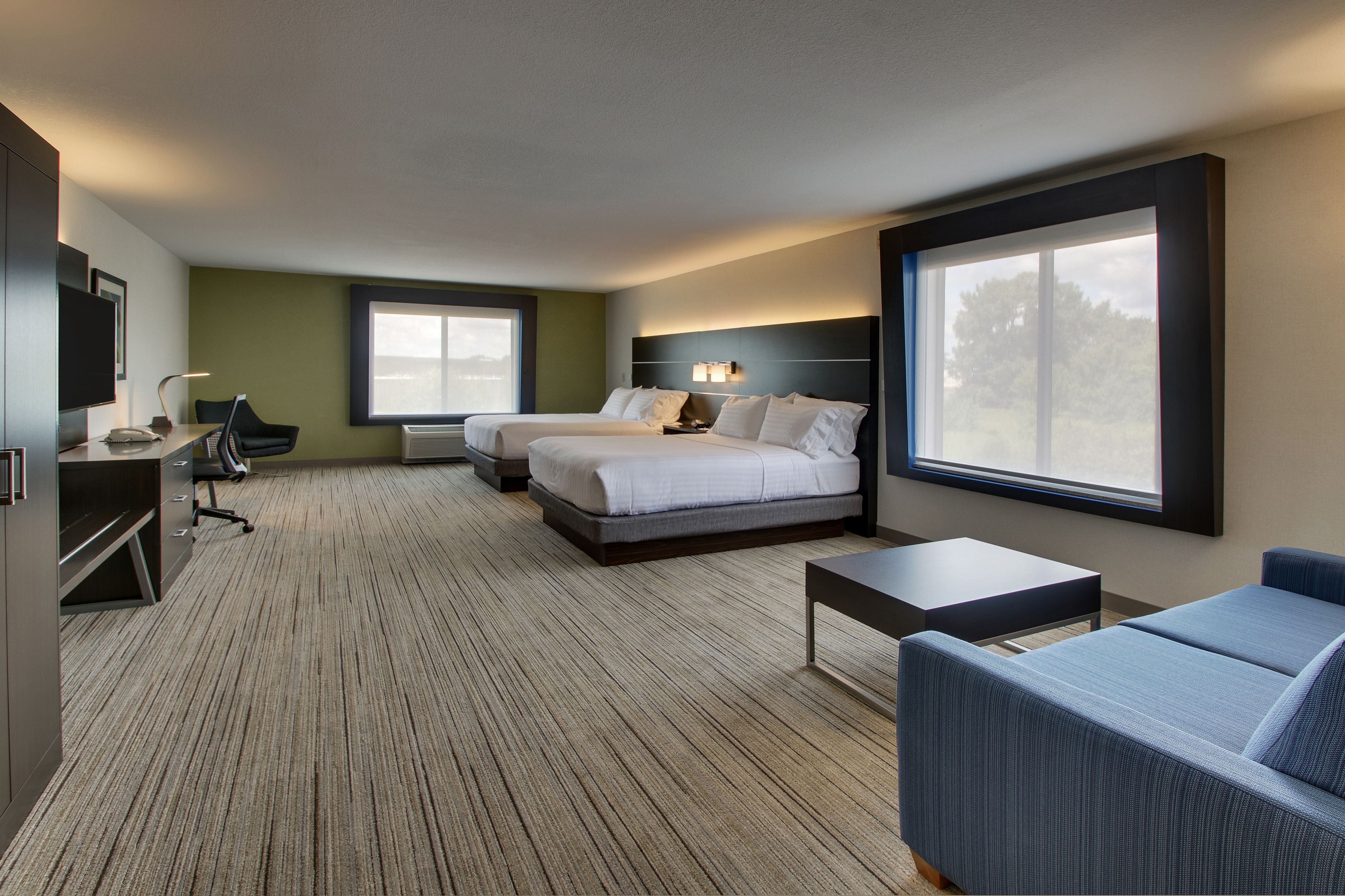 A modern hotel room with two beds, a desk, a chair, and a sofa.