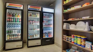 A vending area with two beverage dispensers and a shelf stocked with snacks and condiments.