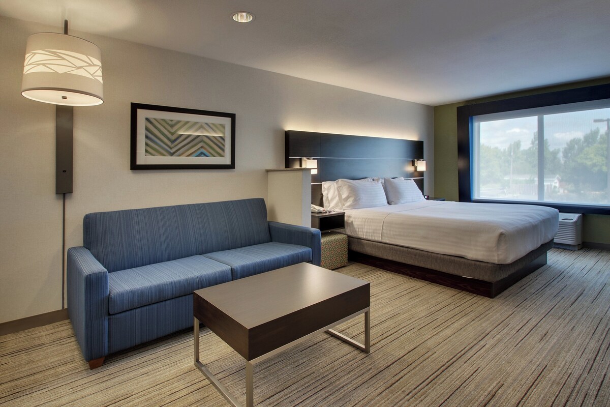 Une chambre d’hôtel avec un lit, un canapé, une table basse, une lampe et un tableau encadré au mur.