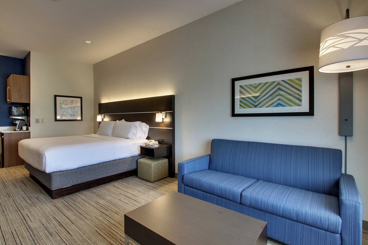 Una habitación de hotel con cama, sofá, mesita de noche, lámpara y un cuadro en la pared.