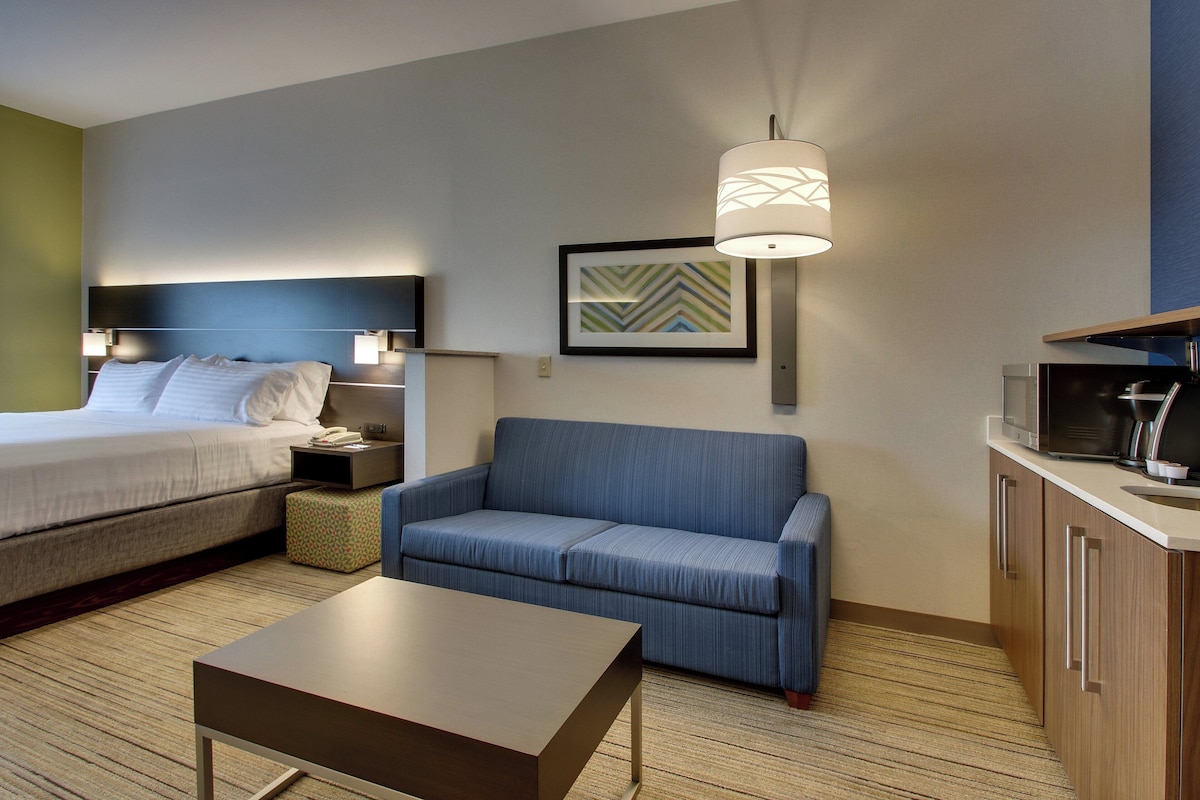 Habitación de hotel con cama, sofá, una mesita, televisor y microondas.