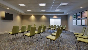 A conference room with rows of chairs, a flat-screen TV, a patterned carpet, and framed artwork on the walls.