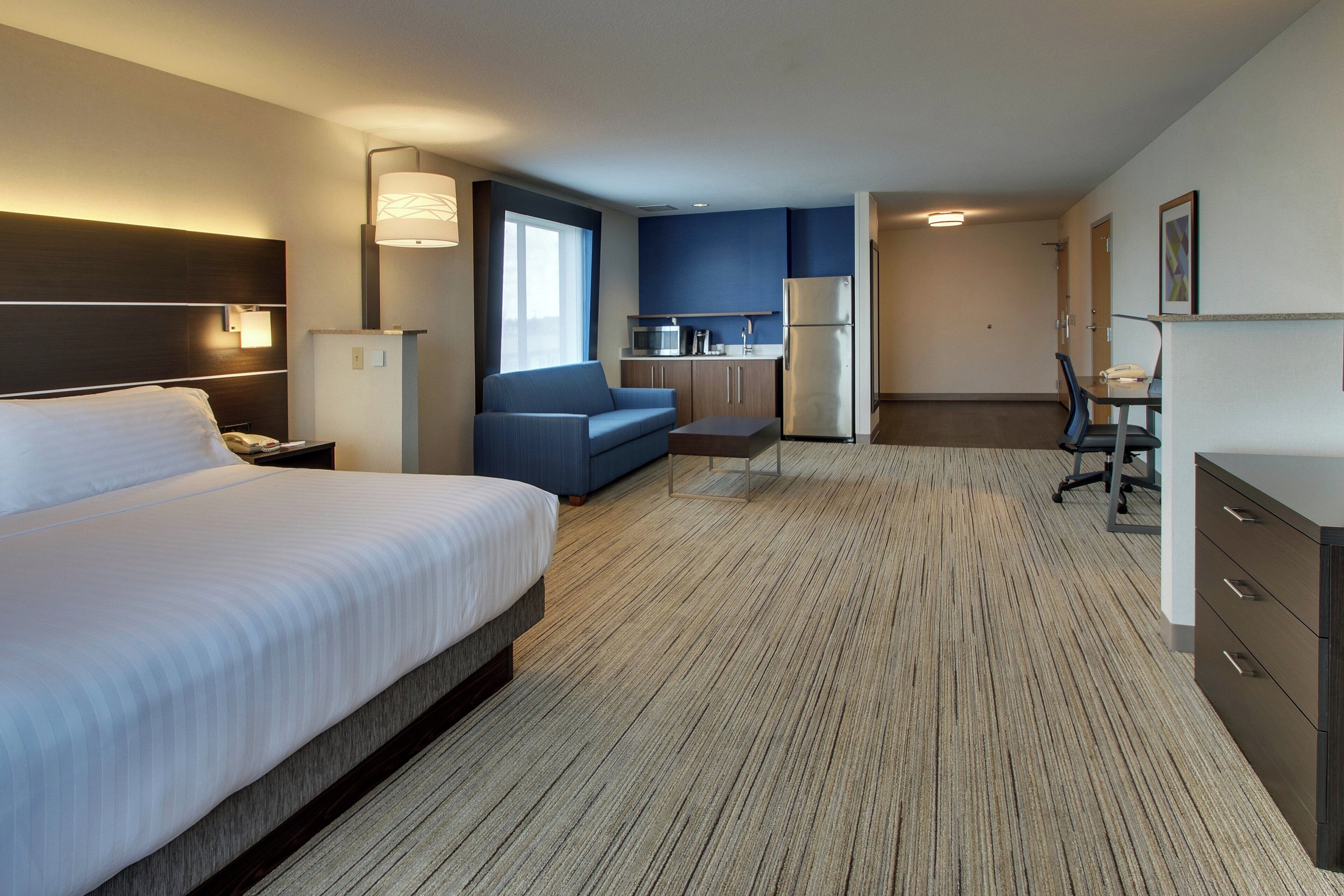 A hotel room with a large bed, a sofa, a kitchenette, and a desk.