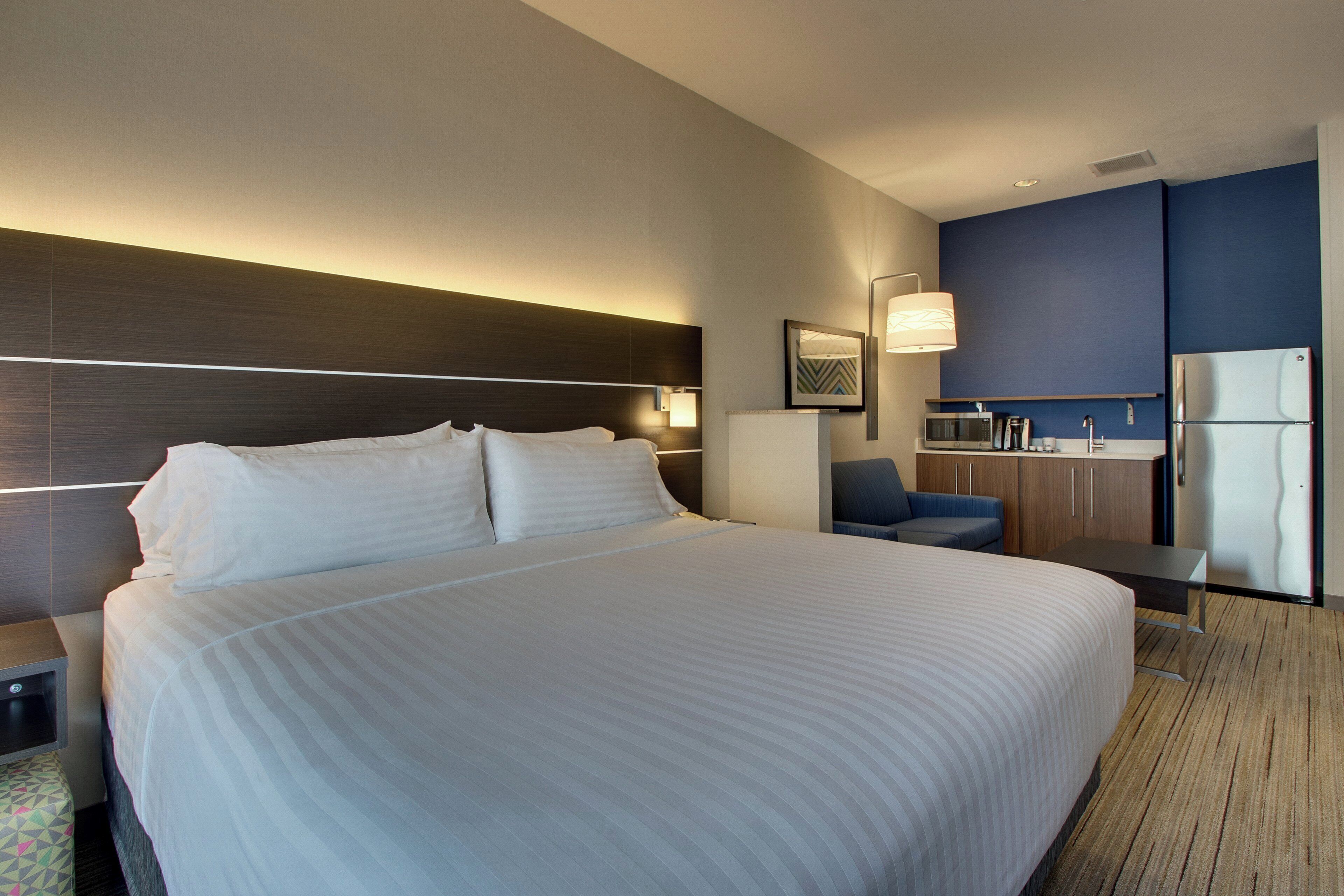 Una habitación de hotel con una cama grande, un escritorio, una silla, una kitchenette y un microondas.