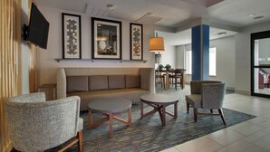 Un hall d’entrée comprenant un canapé, deux fauteuils, une table basse, des œuvres d’art encadrées, un téléviseur et une moquette à motifs.