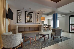 A lobby with a sofa, two armchairs, a coffee table, framed artwork, a television, and a patterned carpet. - Holiday Inn Express & Suites Morris by IHG (Morris)