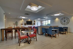 A modern dining area with multiple tables and chairs, recessed ceiling lights, and a large wall clock.