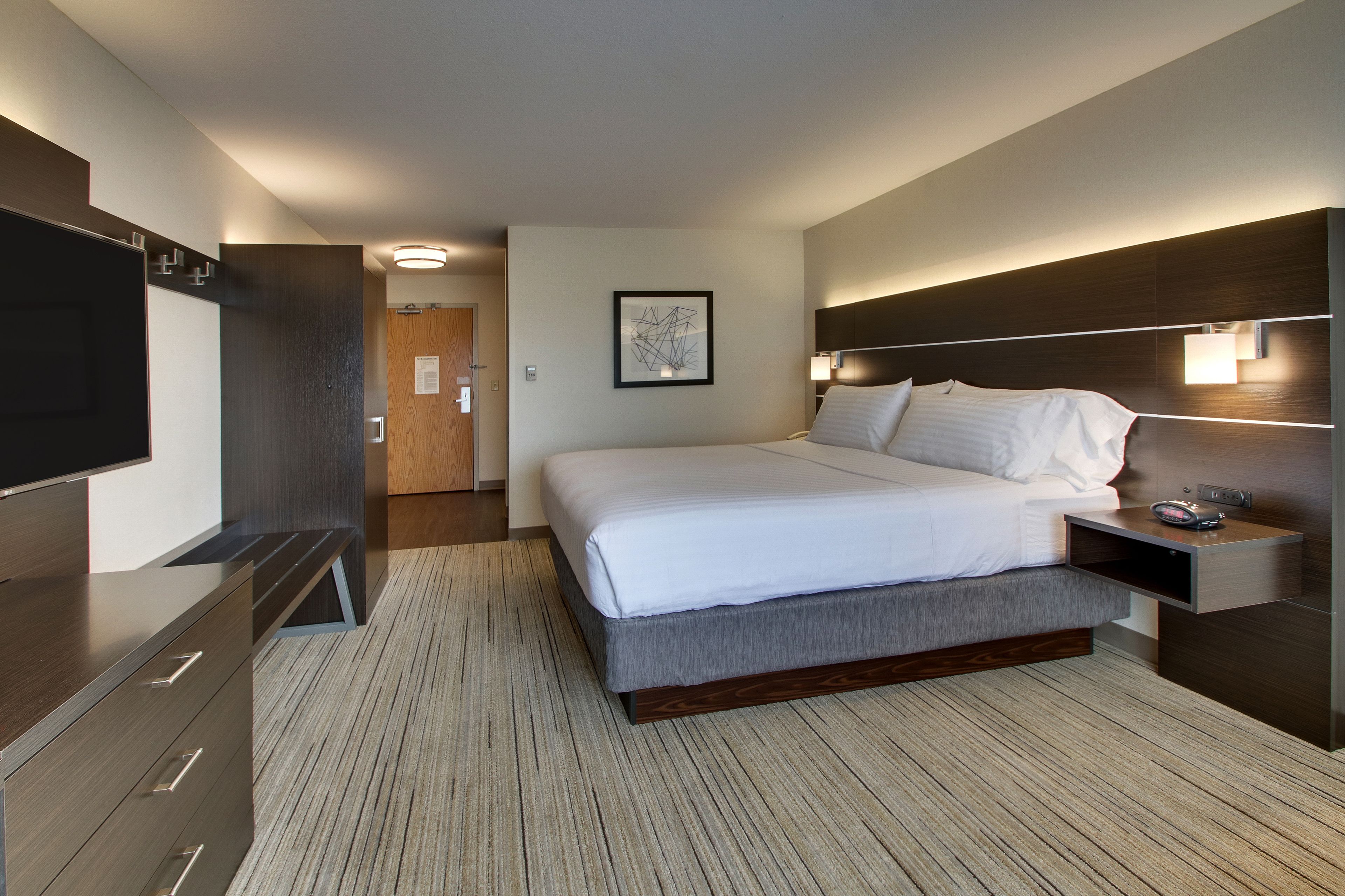 A modern hotel room with a large bed, bedside tables, a flat-screen TV, and a framed picture on the wall.