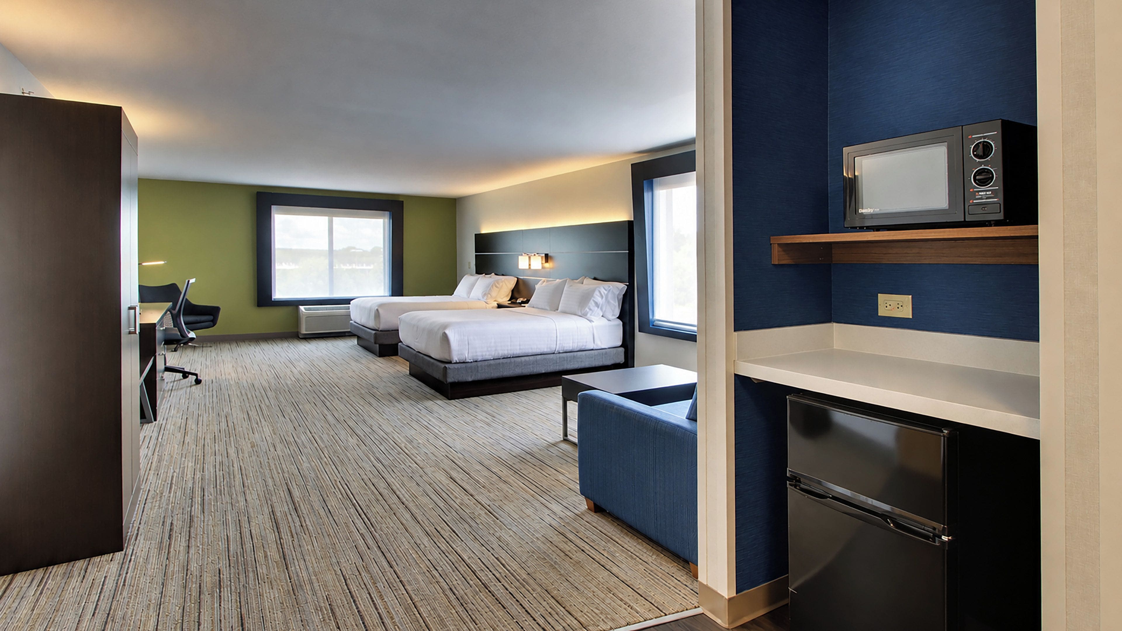 A hotel room with a bed, a desk, a chair, a microwave, and a refrigerator.
