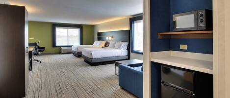 A hotel room with a bed, a desk, a chair, a microwave, and a refrigerator.