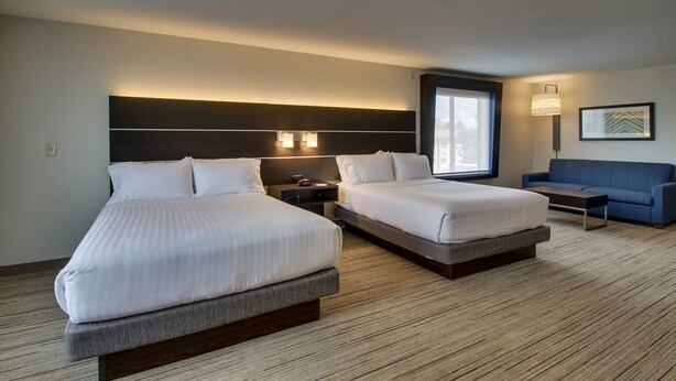 Une chambre d’hôtel avec deux lits, un canapé, une table de chevet et une lampe fixée au mur.