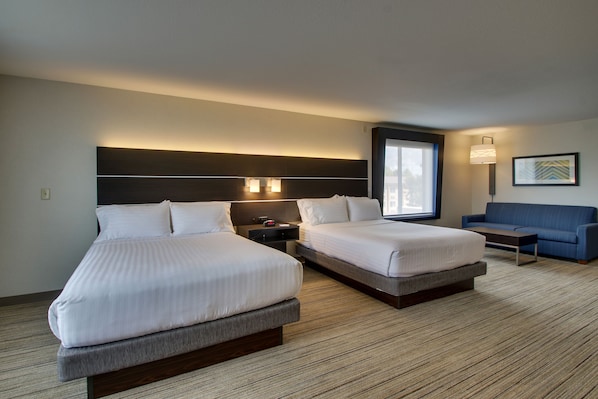 Una habitación de hotel con dos camas, un sofá, una mesita de noche y una lámpara en la pared.