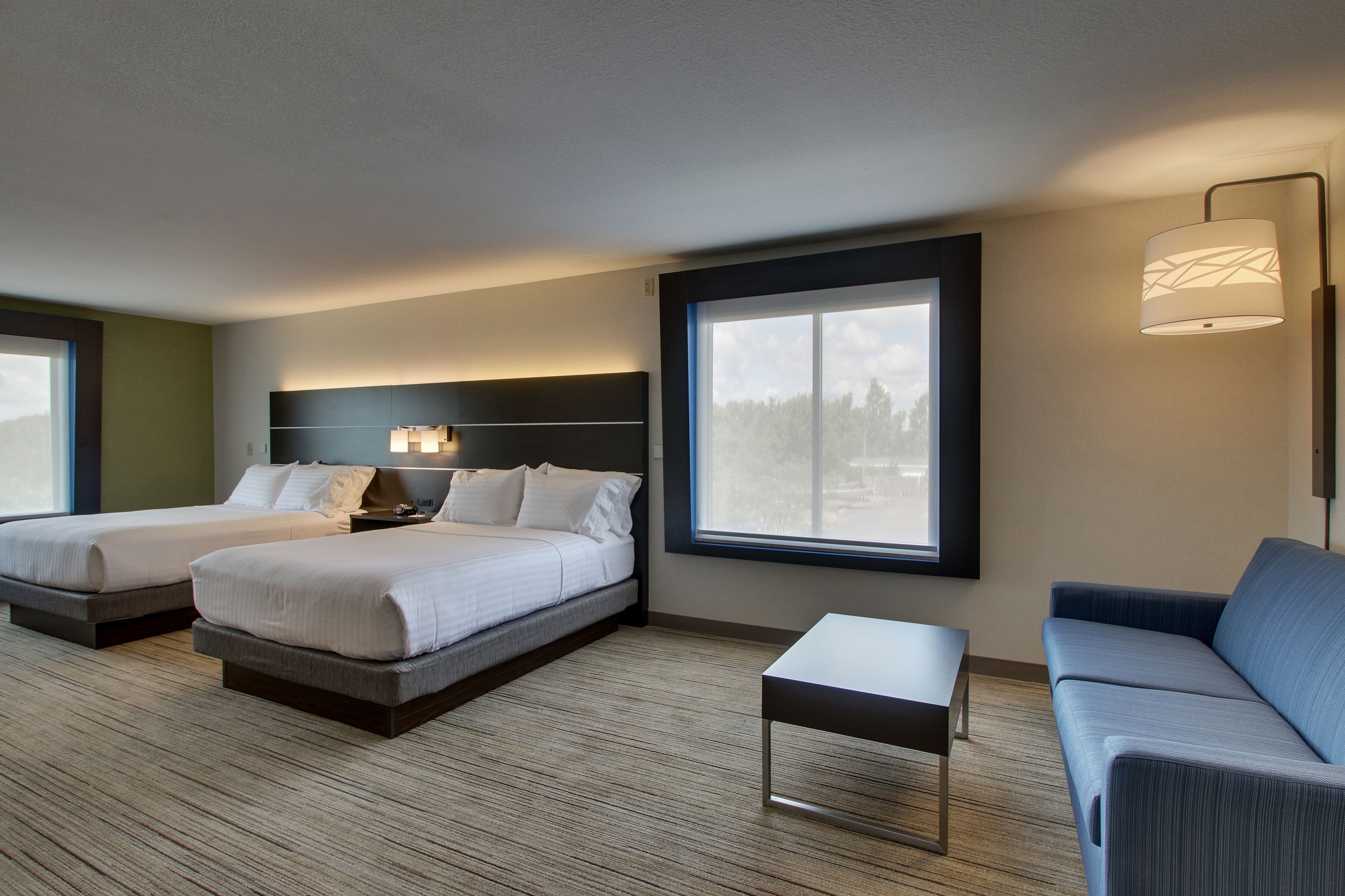 A hotel room with two beds, a sofa, a small table, and a large window.