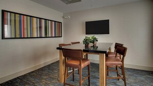 Une salle de conférence équipée d’une table, de quatre chaises, d’un téléviseur à écran plat et d’une peinture abstraite aux couleurs vives accrochée au mur.