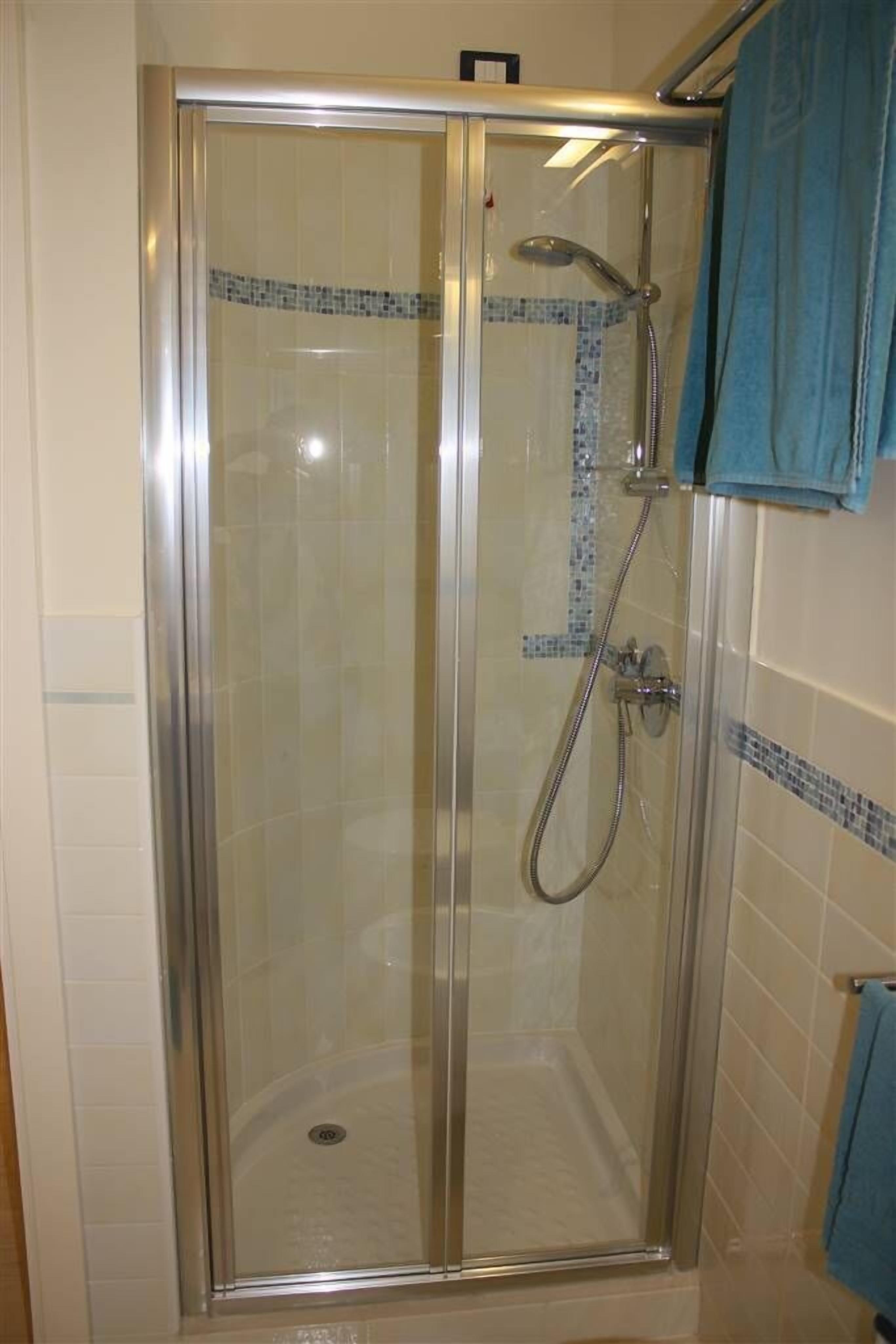 A glass-enclosed shower stall with a handheld showerhead and a wall-mounted faucet.