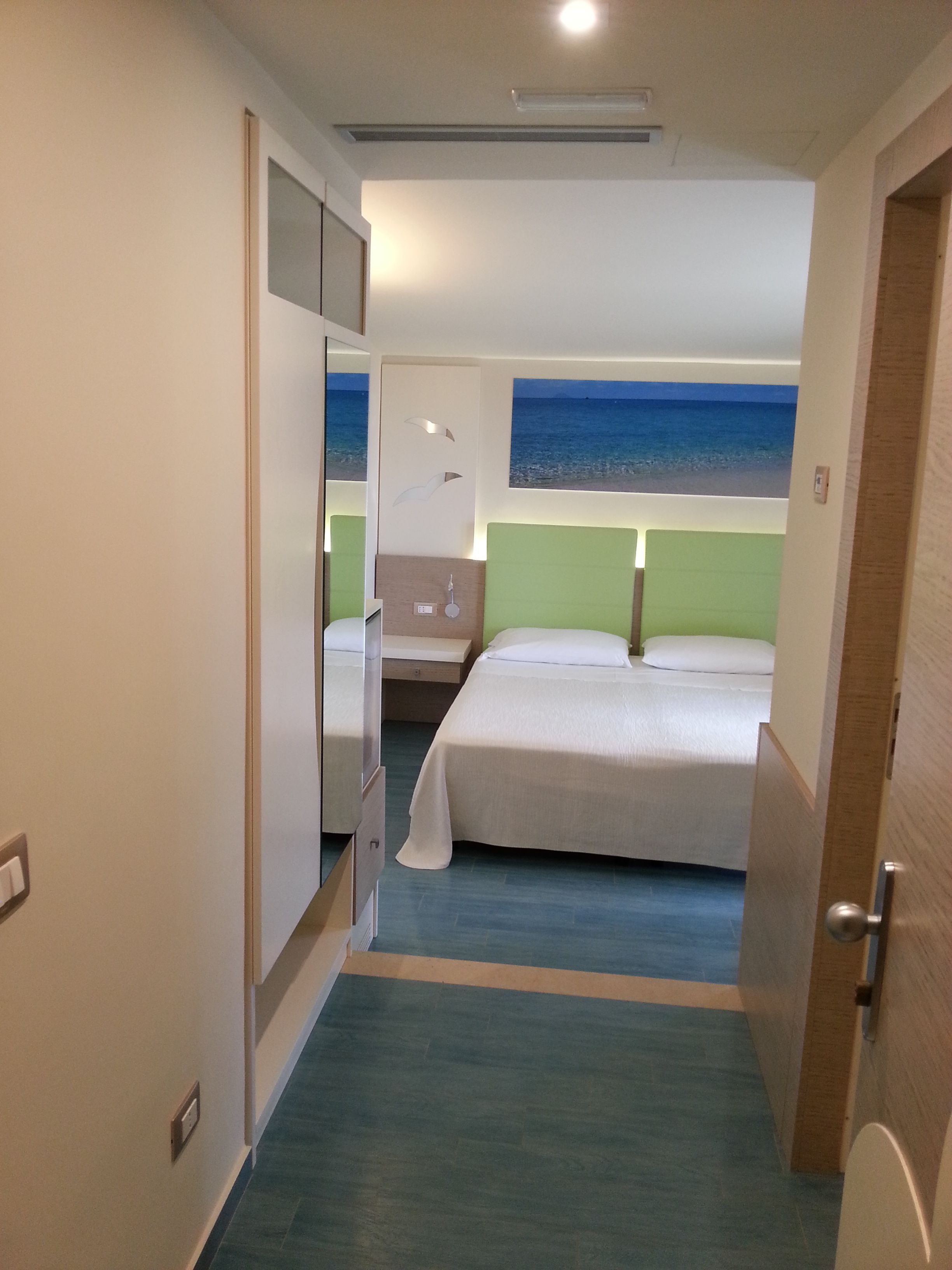 Une chambre d’hôtel avec un lit, une table de chevet, un miroir et une vue sur la mer par la fenêtre.