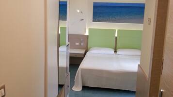 Une chambre d’hôtel avec un lit, une table de chevet, un miroir et une vue sur la mer par la fenêtre.