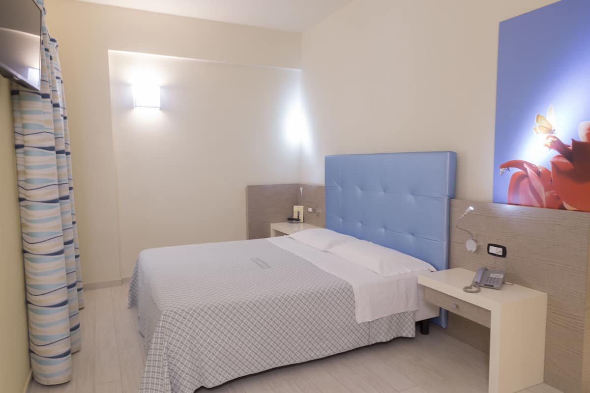 A hotel room with a bed, bedside tables, a desk, a telephone, and a wall-mounted light.