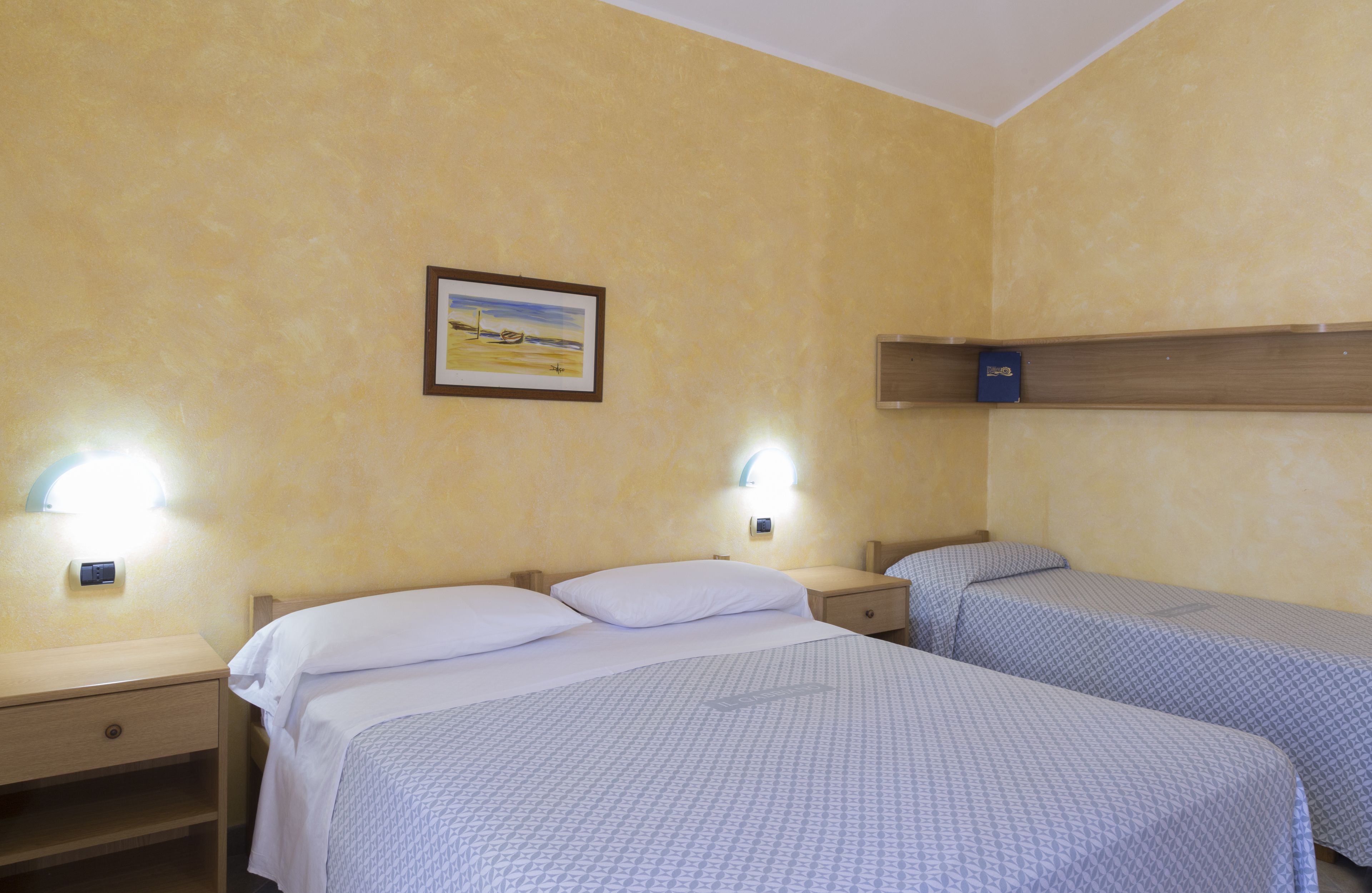 Ein Hotelzimmer mit zwei Betten, einem Nachttisch, einer Ablagefläche an der Wand und einem gerahmten Bild.
