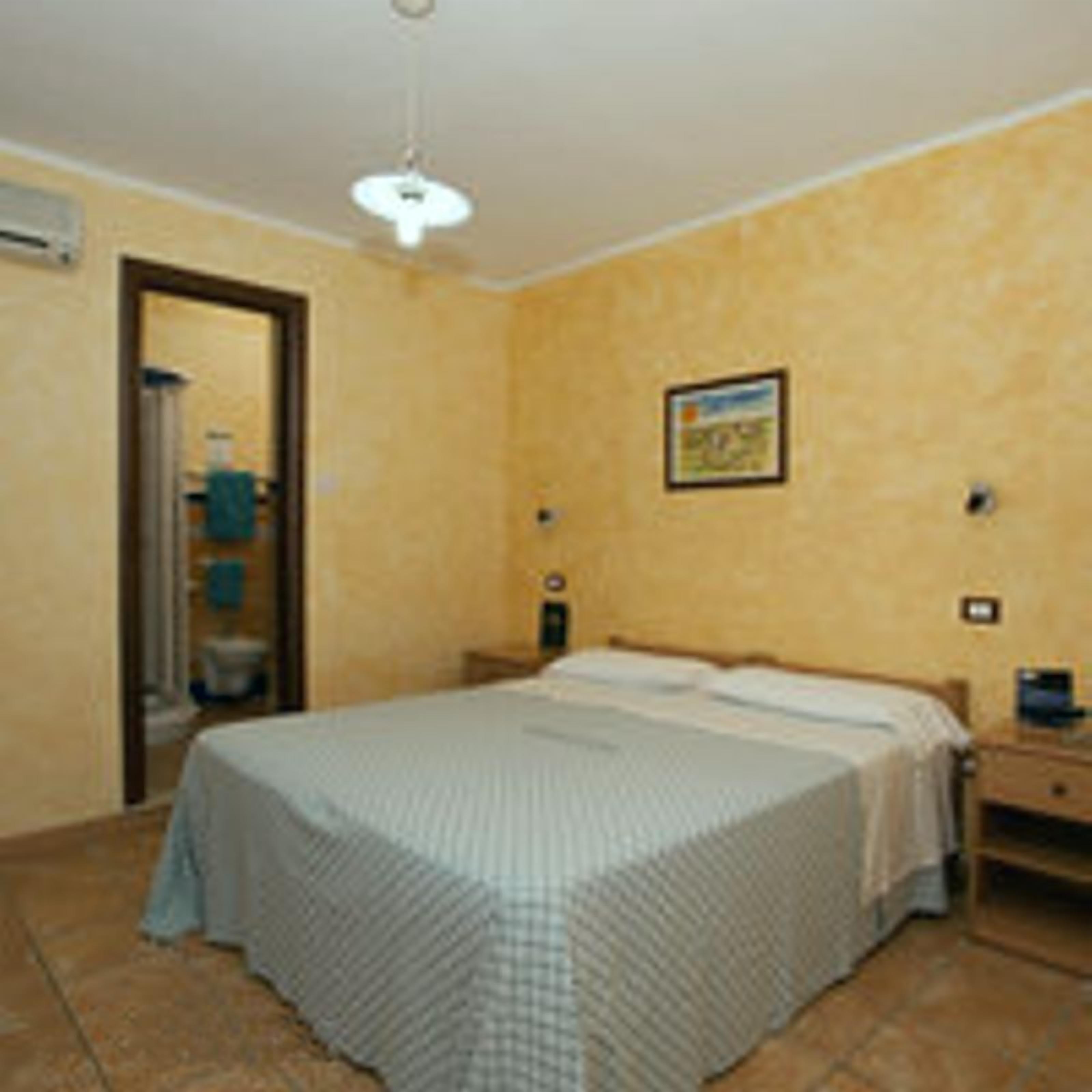A bedroom with a bed, a nightstand, a wall-mounted light, and a door leading to a bathroom.