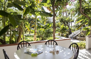 A round table with four chairs, surrounded by lush greenery and a stone pathway. - Villaggio Il Gabbiano (Ricadi)