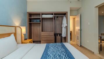 Habitación de hotel con cama, armario de madera, mesita de noche y baño visible a través de una puerta abierta.