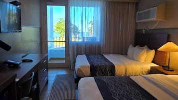 A hotel room with two beds, a desk, a TV, and a balcony with a view.