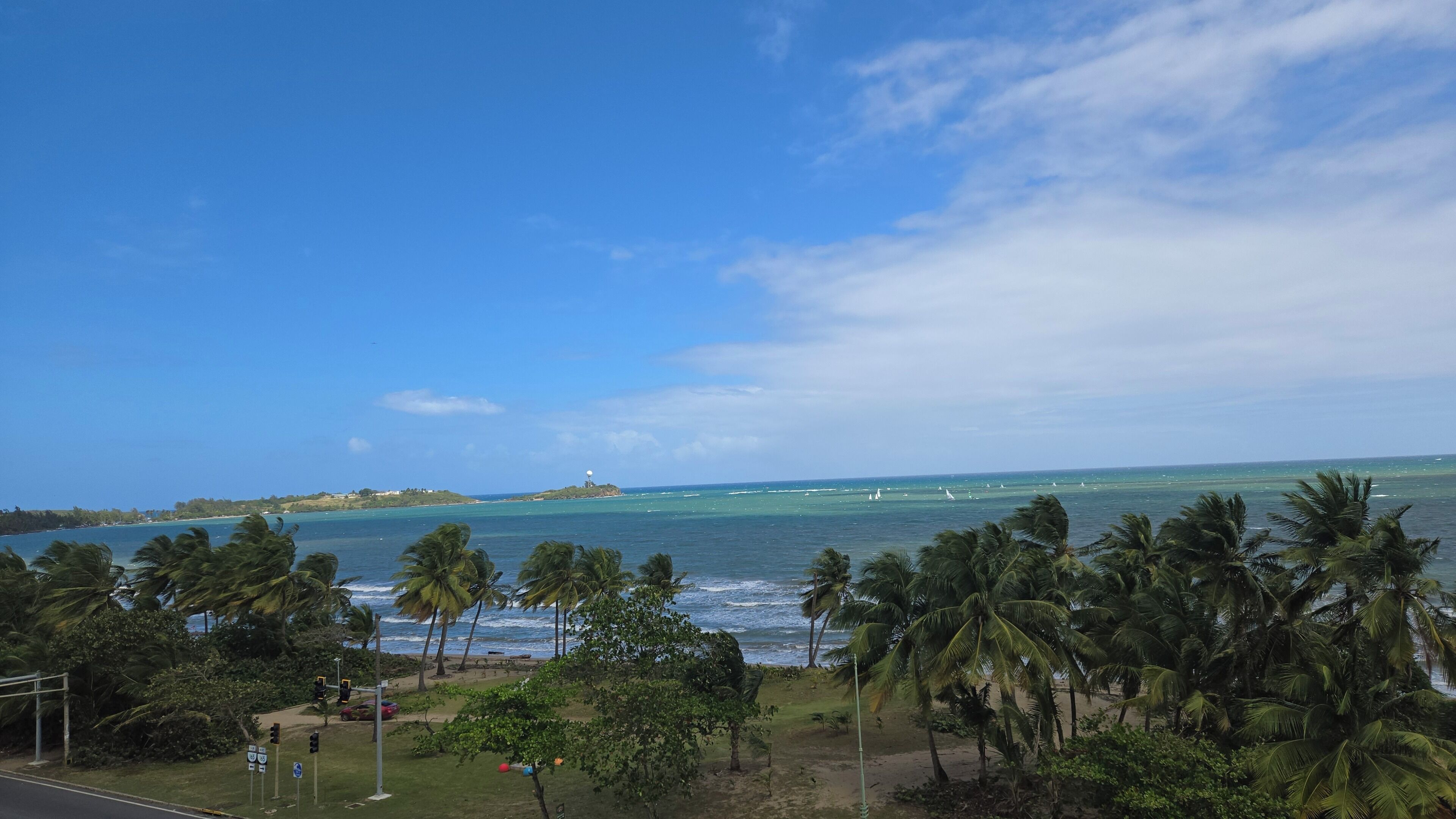 A coastal view with palm trees, a beach, and a lighthouse in the distance.