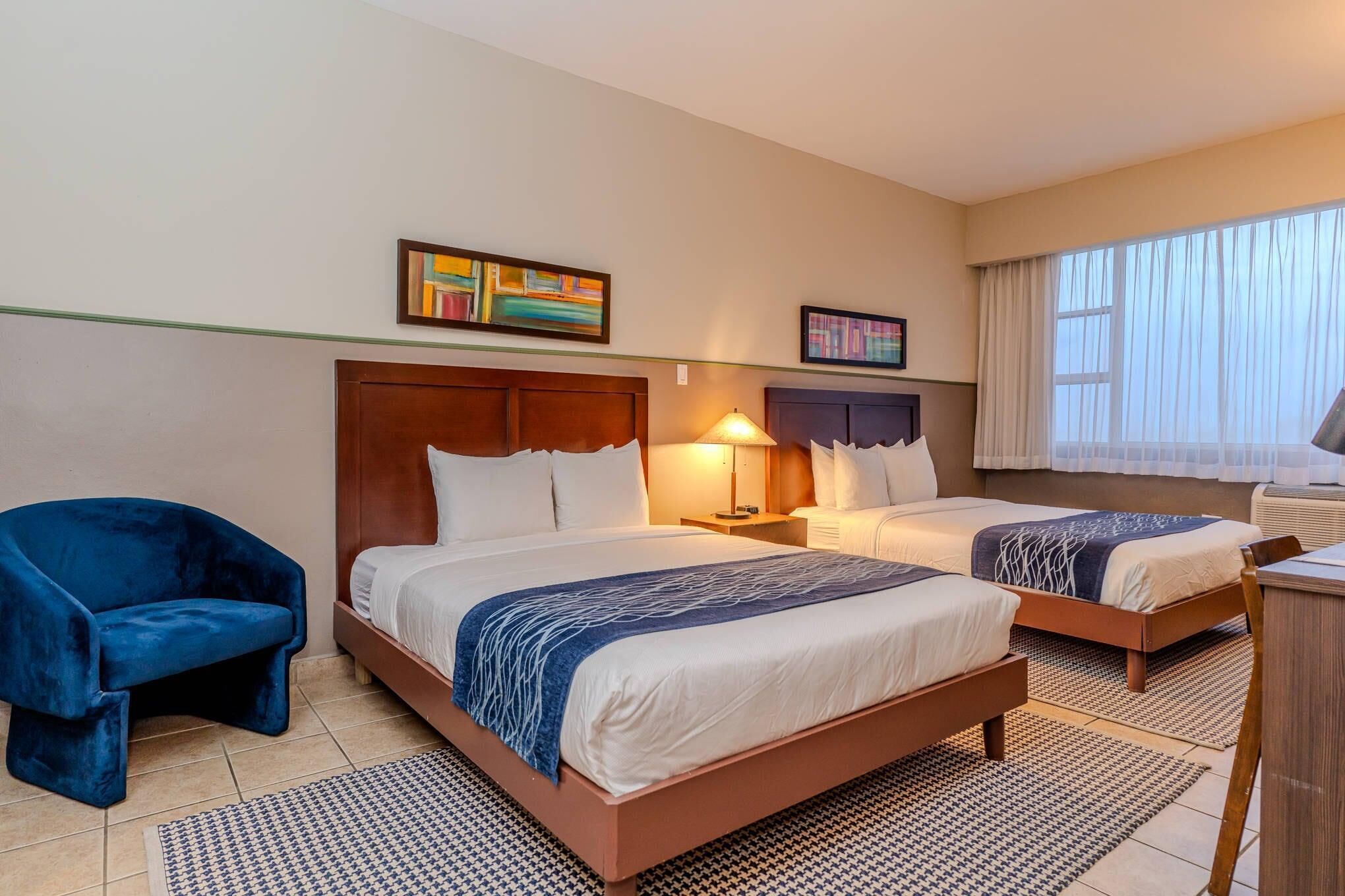 A hotel room with two beds, a blue chair, and artwork on the walls.