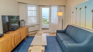 A modern living room with a flat-screen TV, wooden cabinet, blue sofa, and a large painting of palm trees. - Comfort Inn & Suites Levittown (Toa Baja)